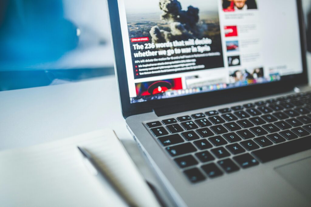 Open laptop displaying an online news article on a desk with a notebook nearby.